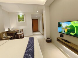 A hotel room with a bed, a desk with a chair, a television on the wall, and a small trash bin.