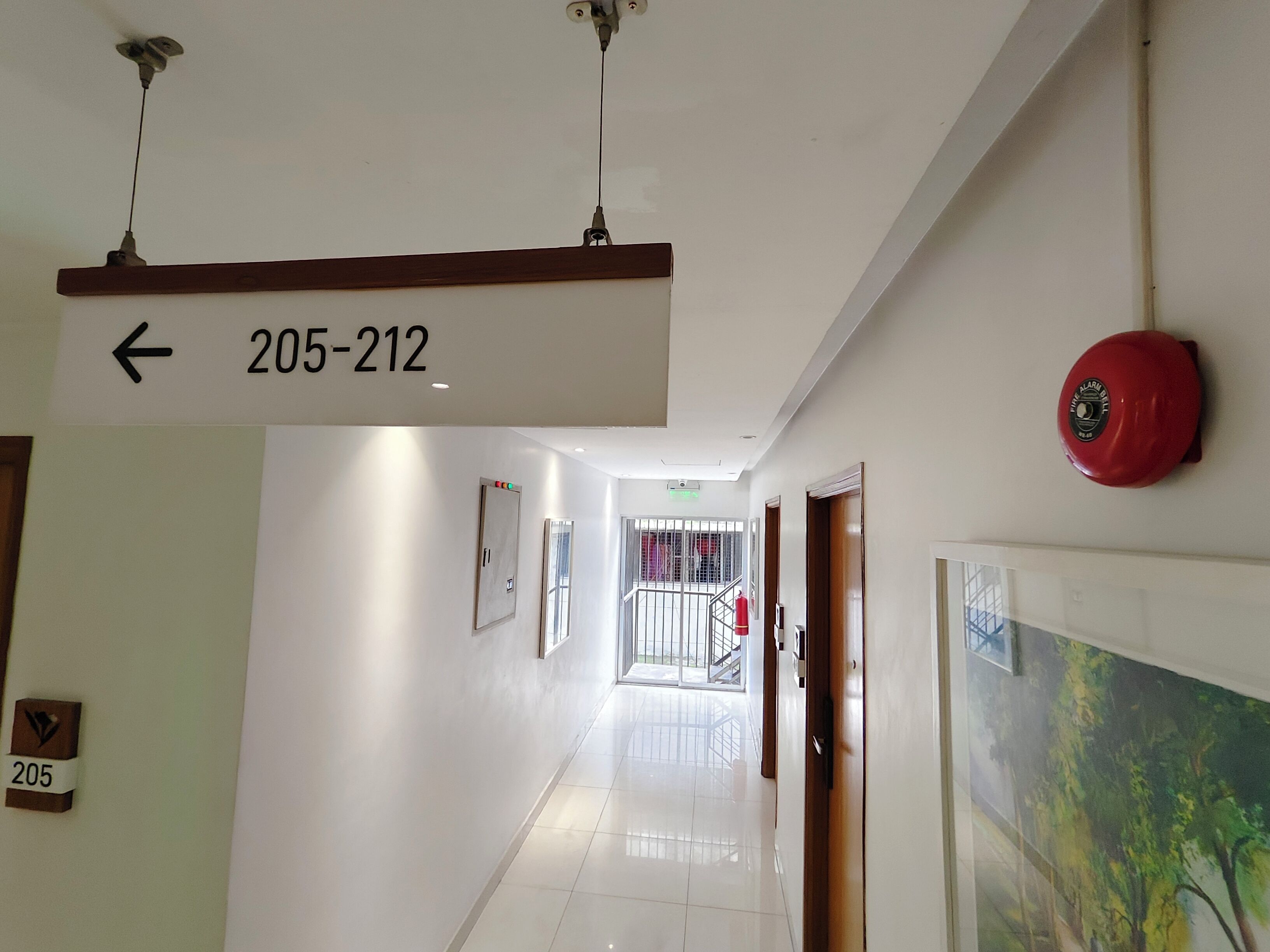 Un pasillo de hotel con un cartel que indica los números de habitación 205 al 212, un extintor y una puerta con cámara de seguridad.