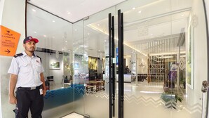 A security guard standing in a modern hotel lobby with glass doors, a reception desk, and a visible restaurant sign. - Hotel Nandini (Dhaka)
