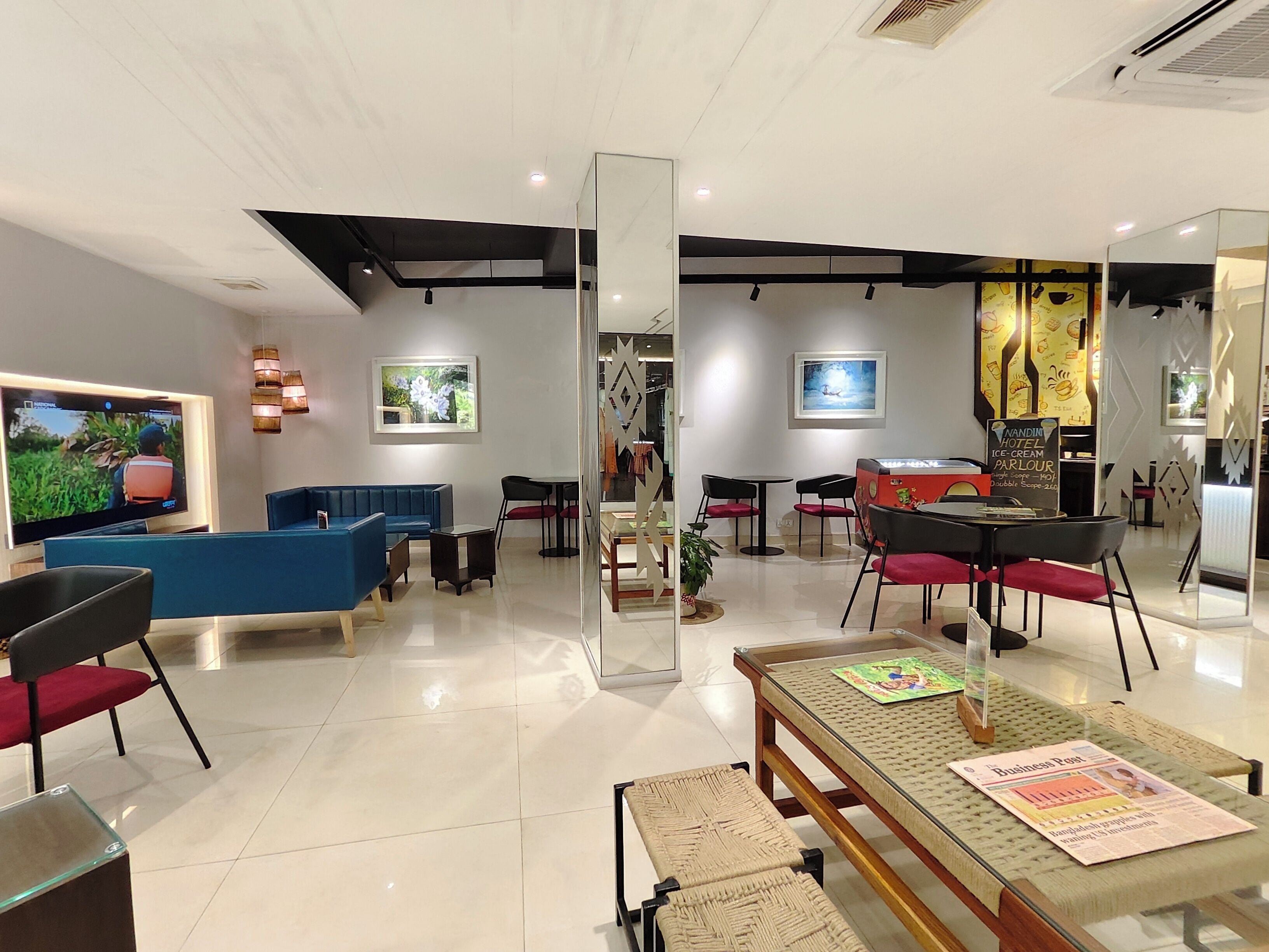 A hotel lobby with a blue sofa, black and red chairs, a wooden coffee table, and a television displaying a nature scene.