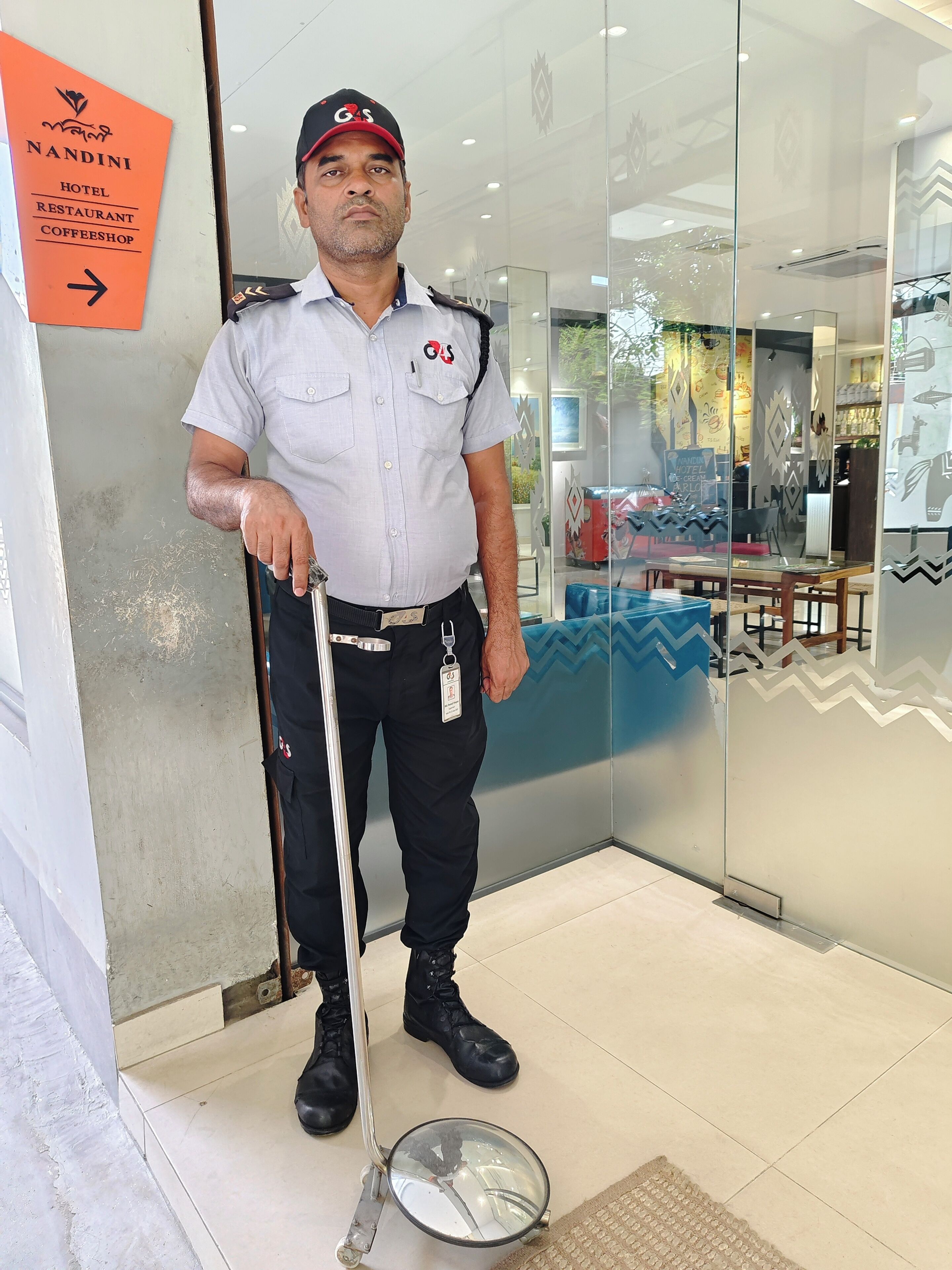 A security guard standing in a hotel lobby with a sign indicating hotel, restaurant, and coffee shop services.