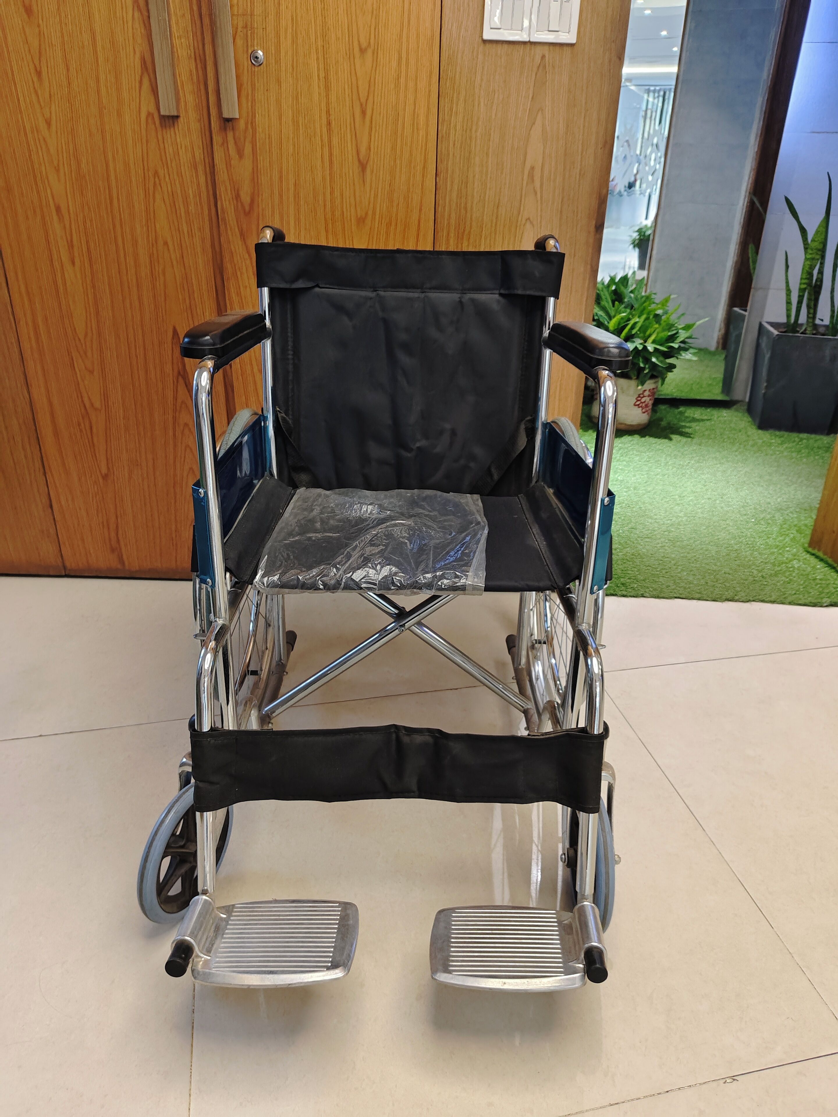 A wheelchair in a room with wooden doors and a potted plant in the background.