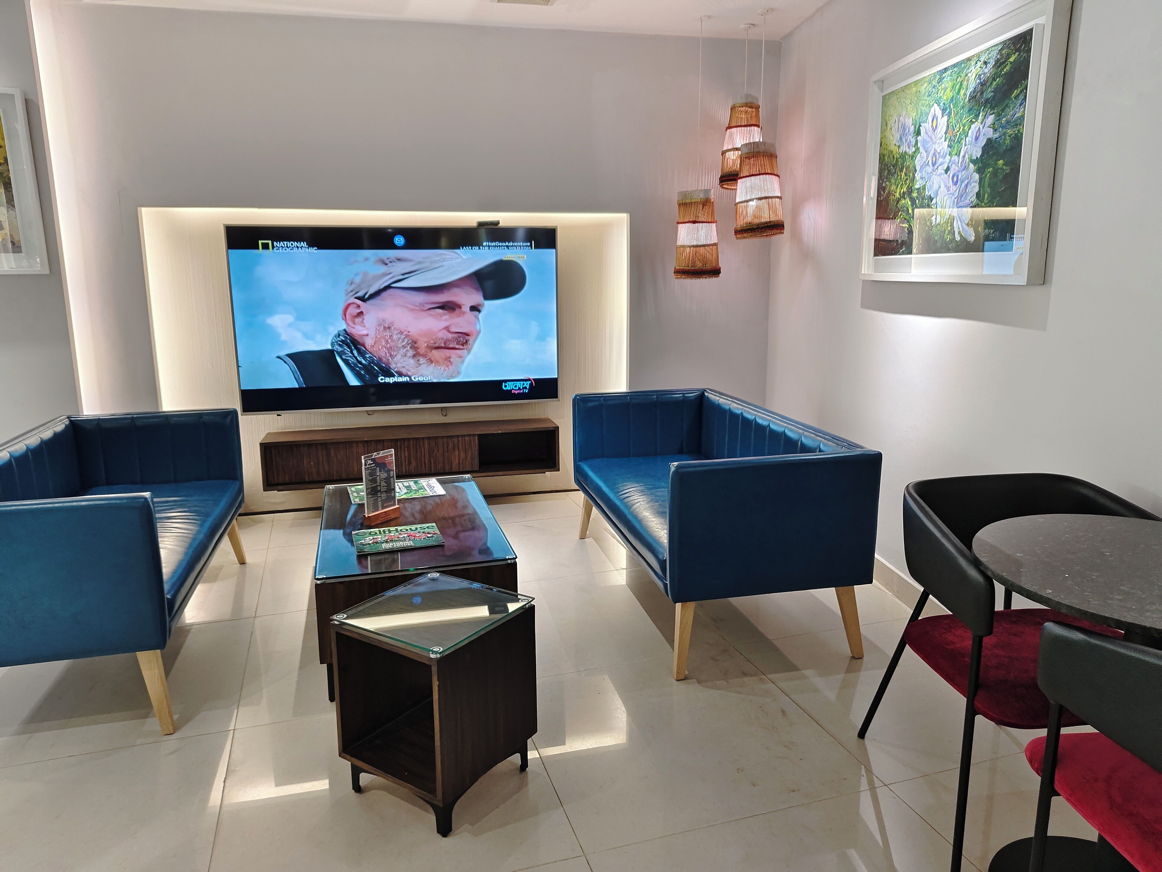 Una sala de estar moderna con televisor de pantalla plana, sofás tapizados en azul, una mesa de centro de vidrio e iluminación colgante.