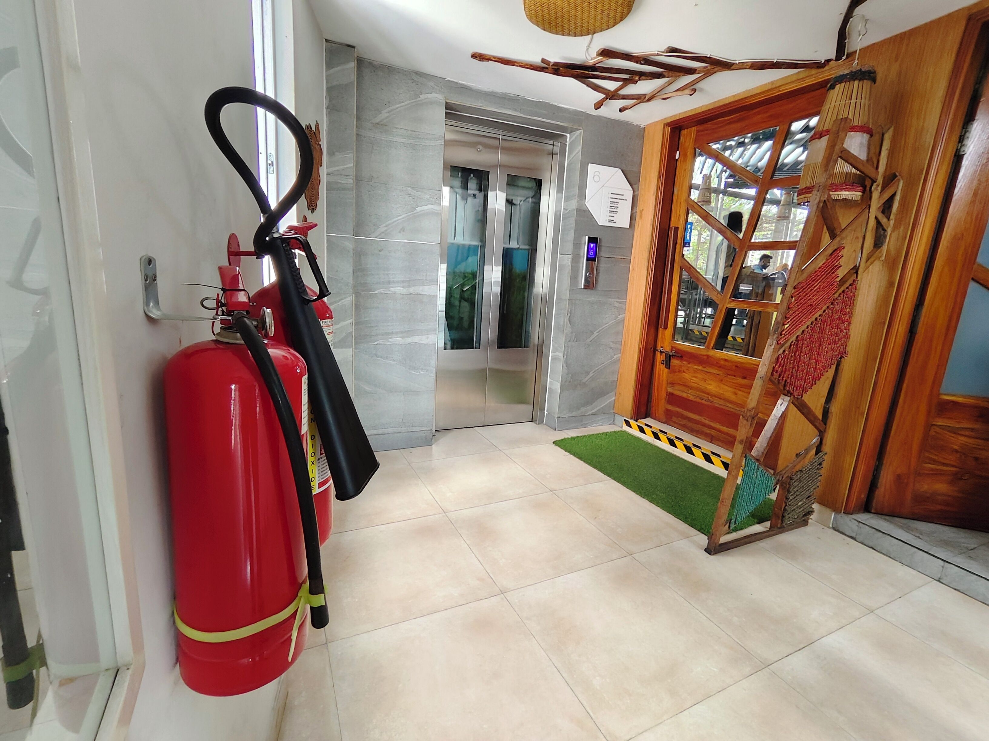 A hallway with a fire extinguisher, an elevator, and a wooden door with a mat.
