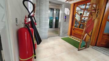 A hallway with a fire extinguisher, an elevator, and a wooden door with a mat.