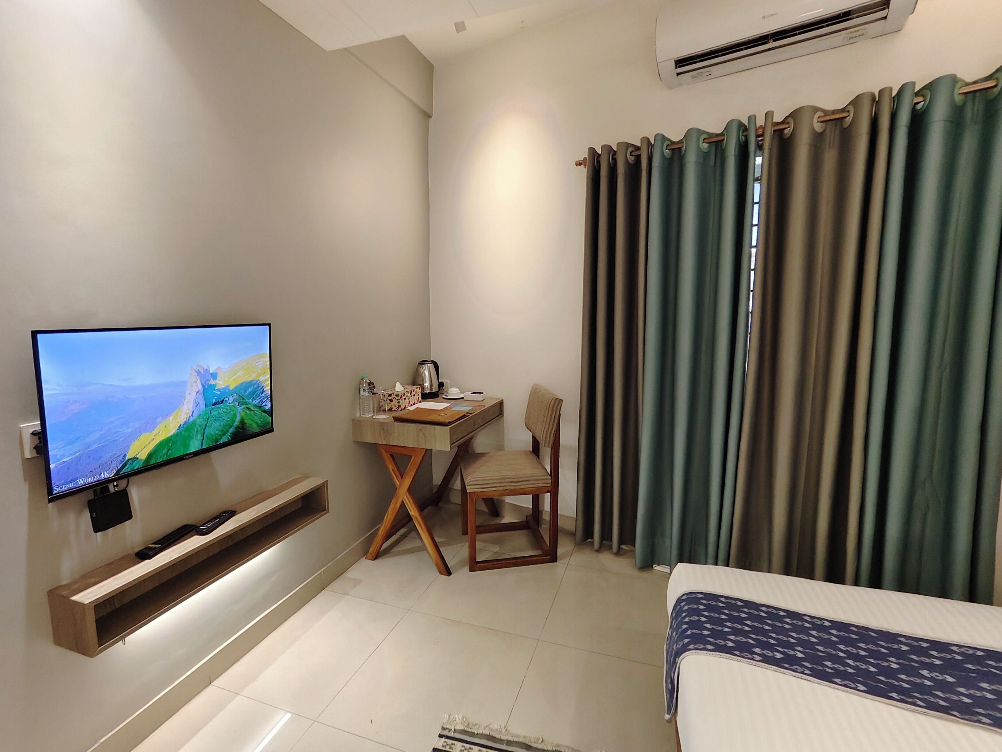 A hotel room with a flat-screen TV, a desk with a chair, a bed, and curtains.