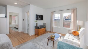 Ein modernes Wohnzimmer mit einer Couch, einem Couchtisch, einem Fernseher und einem Fenster mit Vorhängen.