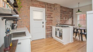 Eine Küche mit Backsteinwand, weißen Schränken, einem eingebauten Backofen und einem Essbereich mit Tisch und Stühlen.