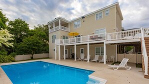 Une maison à deux étages avec une piscine, un patio couvert doté de chaises longues et une cour arrière clôturée.