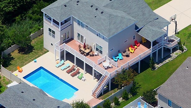 Une maison à deux étages avec une piscine, un patio couvert et un terrain de basket-ball.