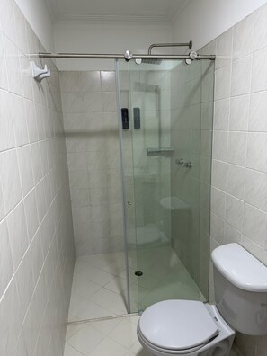 Petita cabina de bany amb porta de vidre, vàter i barana metàl·lica.