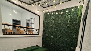 A room with a green artificial grass floor, a wooden bench, and a wall covered in green foliage. - Rustik House (Medellín)
