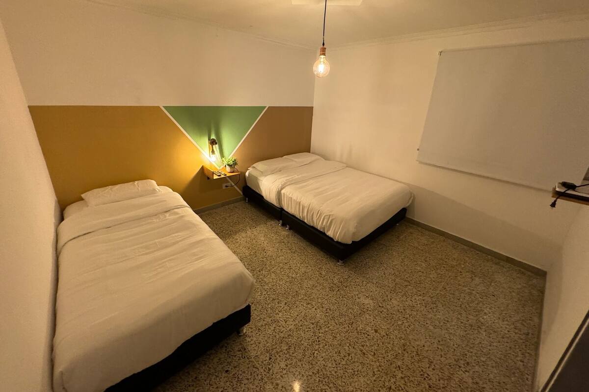 Une petite pièce bien éclairée, avec deux lits simples, un mur d’accent de couleur verte et un luminaire au plafond.