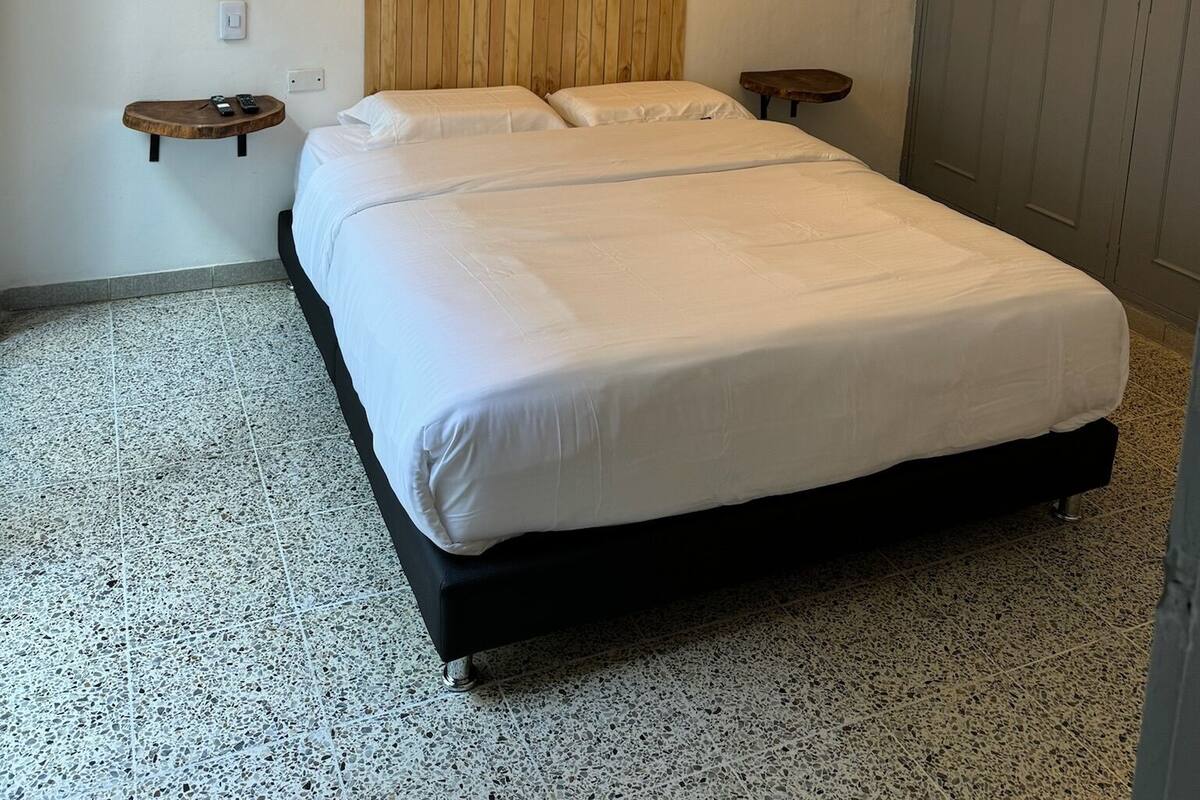 Une chambre à coucher avec un lit, une tête de lit en bois, des lampes suspendues et deux tables de chevet ornées de plantes.