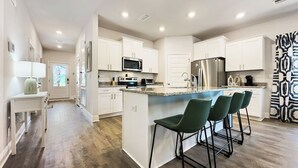 Une cuisine moderne avec des meubles blancs, un îlot central doté de tabourets de bar et un réfrigérateur en acier inoxydable.