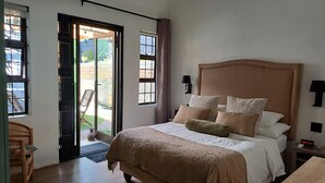 Ein Schlafzimmer mit einem großen Bett, einem Nachttisch, einer Lampe und Blick ins Freie durch eine Schiebetür.