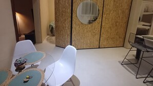 Ein modernes Zimmer mit einer Holzwand, einem runden Spiegel und einem Essbereich mit weißen Stühlen und einem kleinen Tisch.