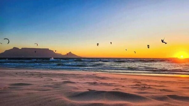 Ein Strand mit fliegenden Drachen, einem Sonnenuntergang und einem entfernten Berg.