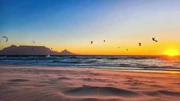 A beach with kites flying, a sunset, and a distant mountain.