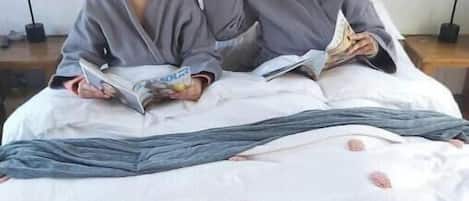 Two people sitting on a bed with a white sheet and pink polka dots, reading a book.