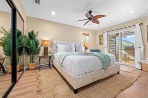 Ein Schlafzimmer mit Bett, Deckenventilator, Topfpflanzen und Blick durch eine Glastür.