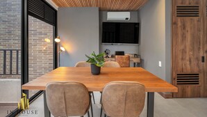 Un coin repas moderne avec une table en bois, deux chaises, une plante en pot et un téléviseur fixé au mur.