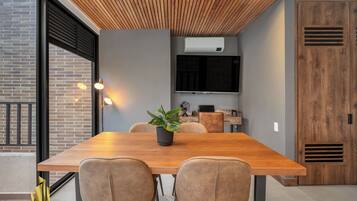 Un comedor moderno con una mesa de madera, dos sillas, una planta en maceta y un televisor en la pared.