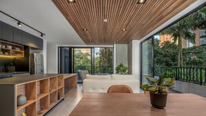 Une cuisine moderne avec un plafond en bois, des étagères intégrées et un coin repas comprenant une grande table et une plante en pot.