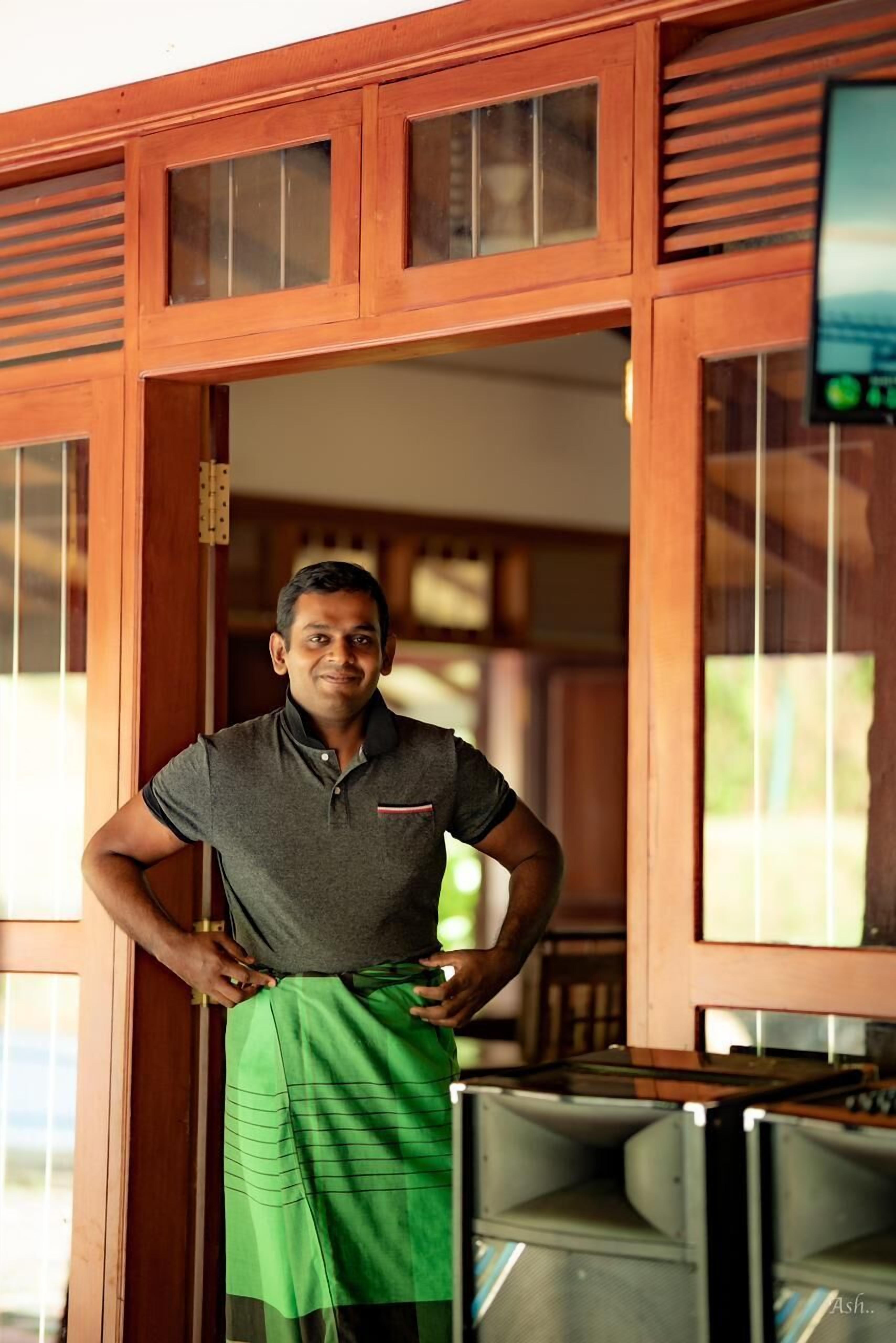 A person standing in a doorway with a green cloth draped over their shoulder, wooden paneling, and a television mounted on the wall.