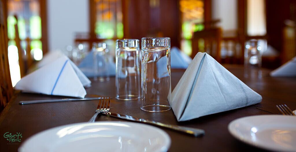A dining table set with white plates, clear glasses, and folded napkins.