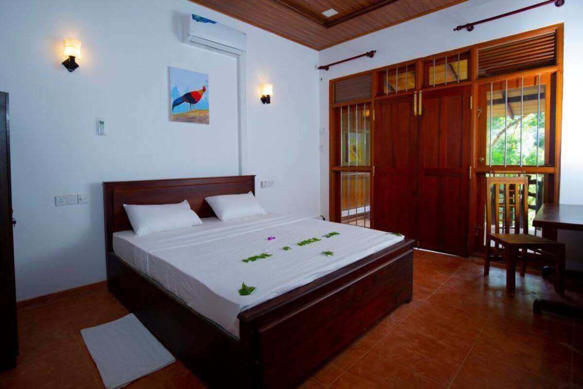 Un dormitorio con una cama de madera, ropa de cama blanca, una alfombra pequeña, un cuadro en la pared y una puerta de madera.