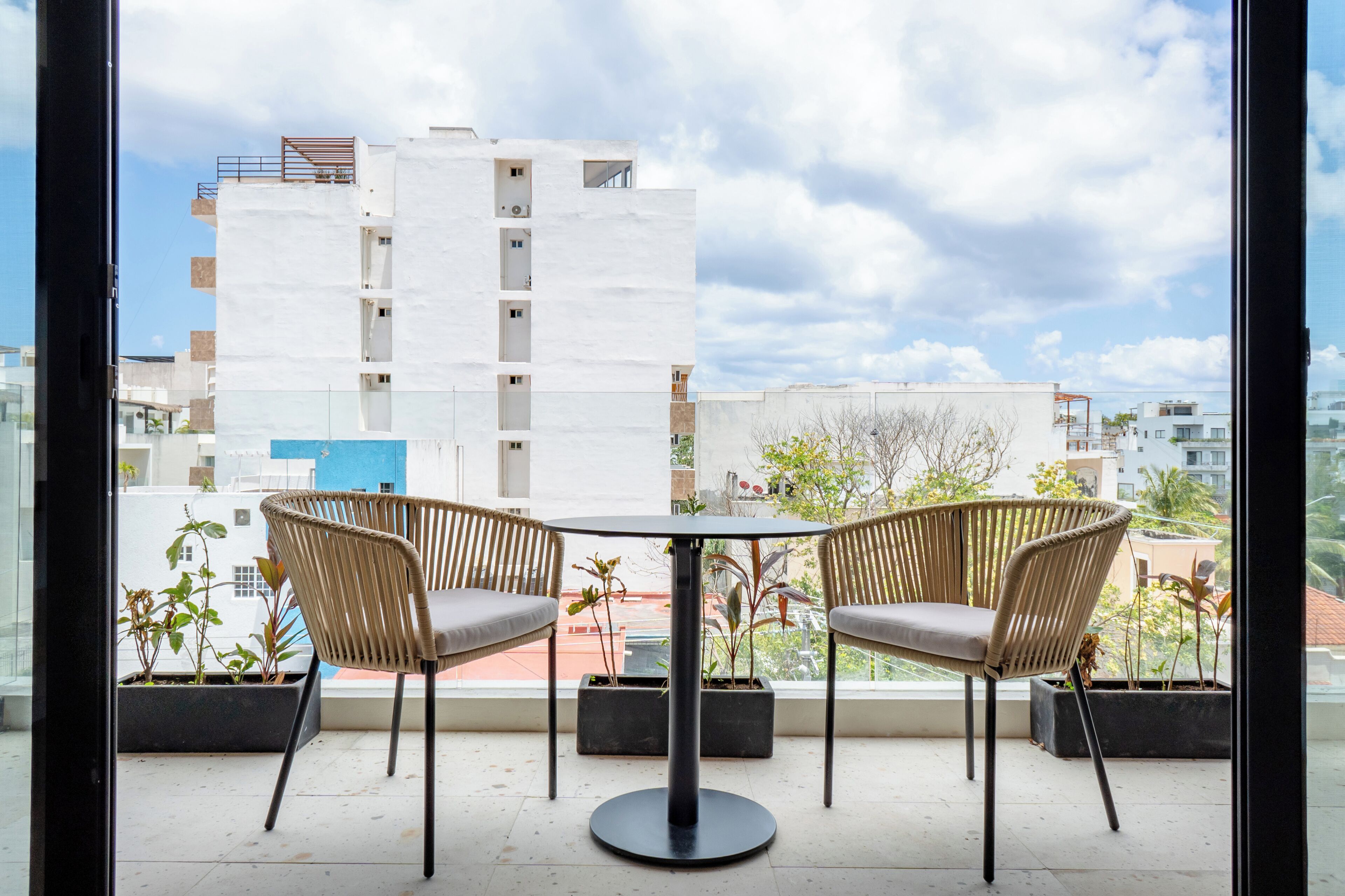 A balcony with two wicker chairs and a table, overlooking a cityscape with modern buildings.