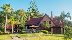 A large house with a stone foundation, a red roof, and a chimney. There is a covered patio area with a table and chairs.