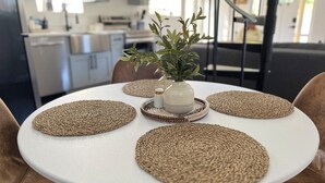 Een ronde eettafel met vier gevlochten placematen en een vaas met groene planten.