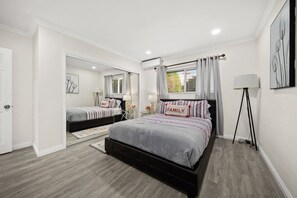 A bedroom with two beds, a large window with curtains, a floor lamp, and a mirror.