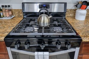 A kitchen with a stainless steel stove, a kettle, and a container labeled 'UTENSILS'.