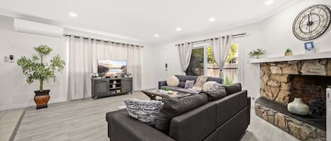 A modern living room with a sofa, a flat-screen TV, a fireplace, and a large window.