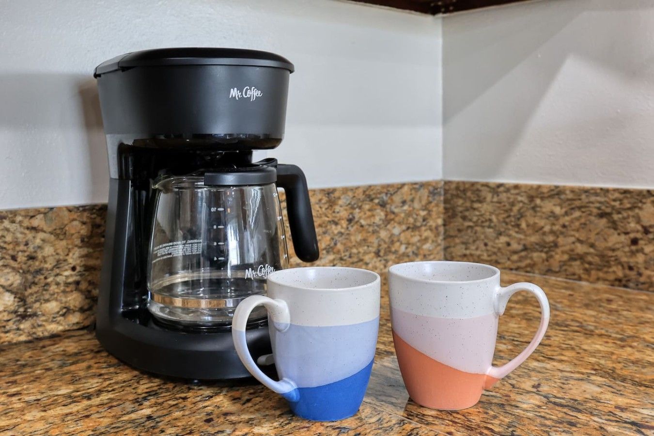En kaffemaskine med to kopper på en bordplade af granit.