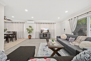 Ein modernes Wohnzimmer mit einem grauen Sofa, einem Couchtisch und einem Fernseher im Hintergrund.