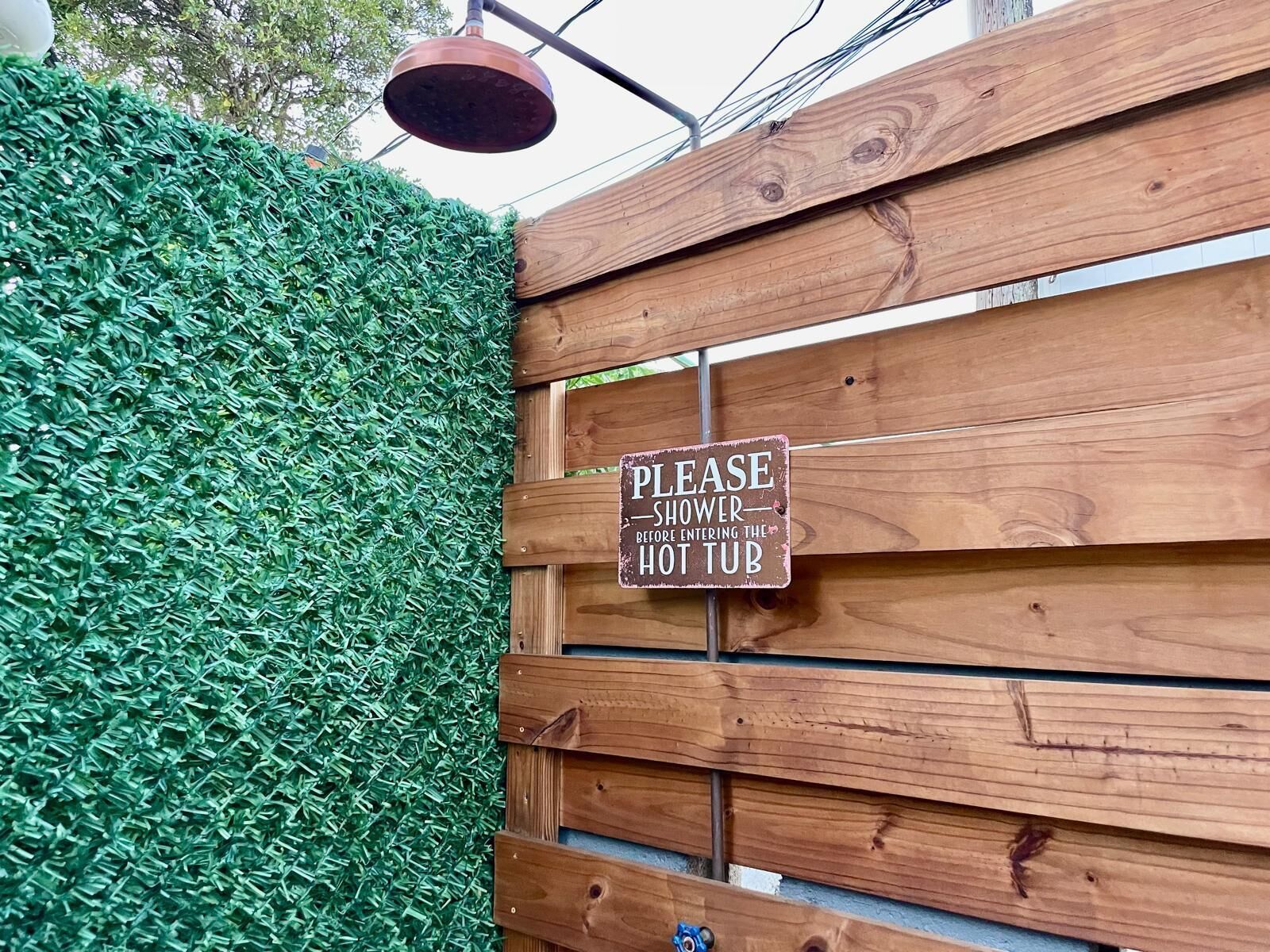 A wooden gate with a sign requesting visitors to shower before entering the hot tub.
