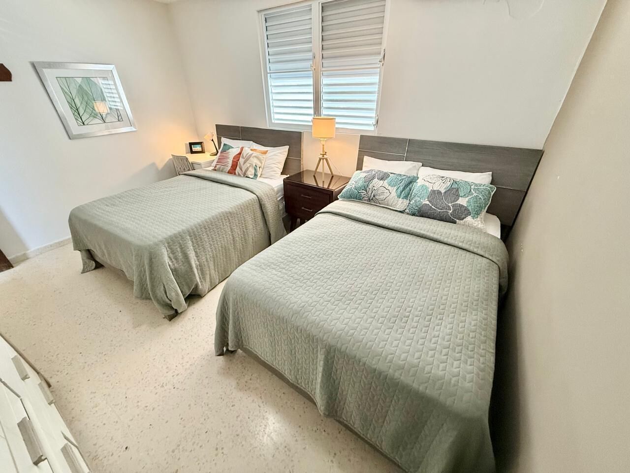 A bedroom with two beds, a nightstand, a lamp, and a framed picture on the wall.