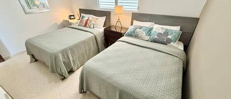 A bedroom with two beds, a nightstand, a lamp, and a framed picture on the wall.