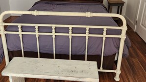 A bedroom with a white metal bed frame, purple bedding, a small bedside table, and a wooden bench. - Cozy 1 bedroom cabin in peaceful Trinity Center with AC (Trinity Center)