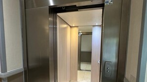 An elevator with a metallic finish, a visible emergency phone, and a tiled floor. - Bel Appartement Aéré et Cosy (Montévrain)