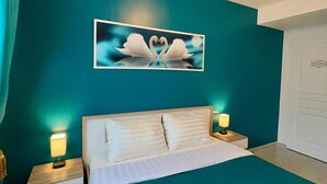 A bedroom with teal walls, a bed with white bedding, two bedside lamps, and a wall-mounted light fixture. - Bel Appartement Aéré et Cosy (Montévrain)