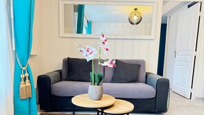 A modern living room with a grey sofa, two round wooden tables, and a potted orchid plant. - Bel Appartement Aéré et Cosy (Montévrain)