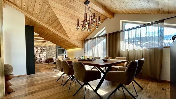 A dining area with a wooden table and chairs, a stone wall, and a large window with curtains. - 350 - Suite The West - Luxury residence (Courchevel)