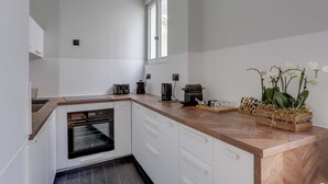 A modern kitchen with white cabinetry, a built-in oven, a coffee maker, and a wooden countertop. - 168 Suite M - Superb apartment in Paris (Paris 02 Bourse)