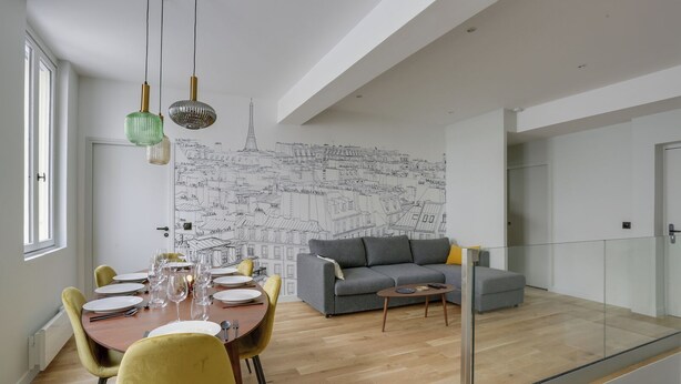 A modern living room with a dining area, a grey sofa, and a cityscape mural on the wall. - 168 Suite M - Superb apartment in Paris (Paris 02 Bourse)
