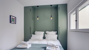 A neatly made bed with white linens and a blue blanket, two bedside lamps, and a framed picture on the wall. - 168 Suite M - Superb apartment in Paris (Paris 02 Bourse)